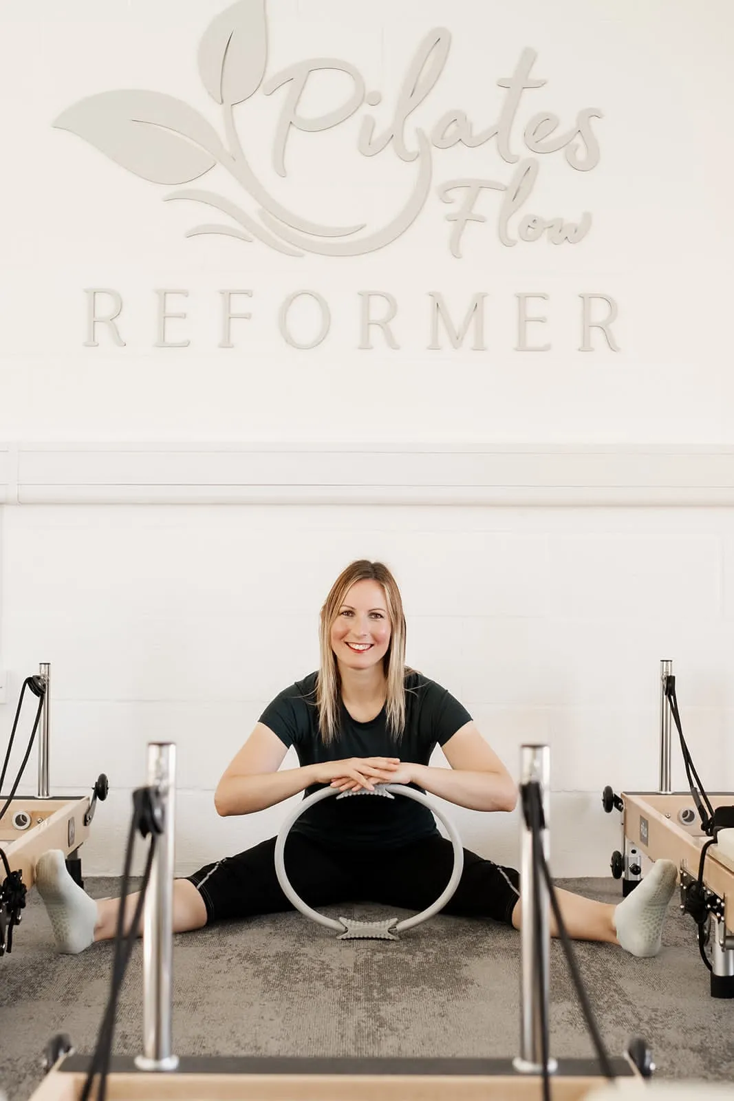 Instructor stretching under the Pilates Flow Reformer logo in the Quedgeley studio