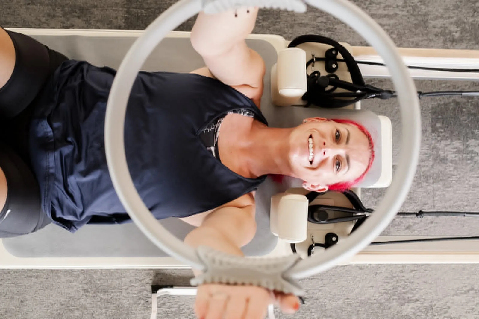 Overhead view of a client smiling through a Pilates ring on the reformer