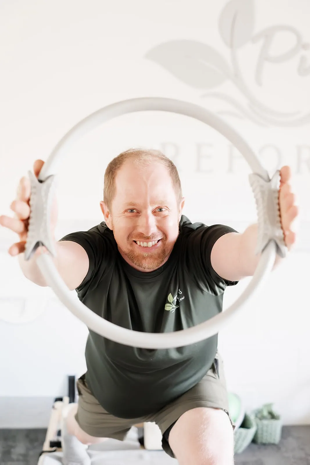 Instructor smiling through a Pilates ring under the studio logo